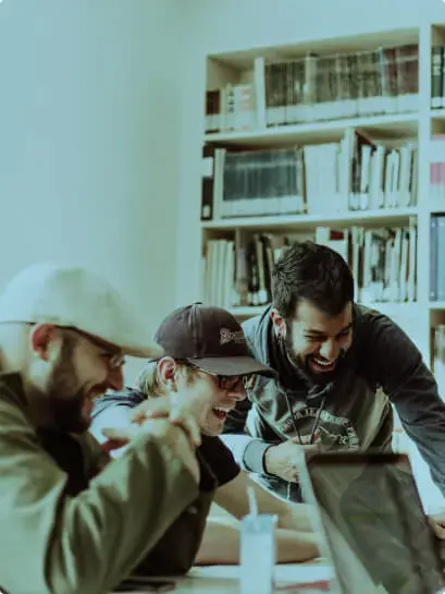 Three people collaborating happily on a laptop in a modern workspace